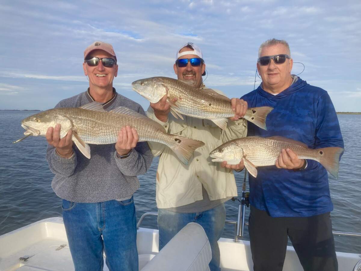 Three people stand on the back of a fishing charter boat and hold up the fish they've caught.