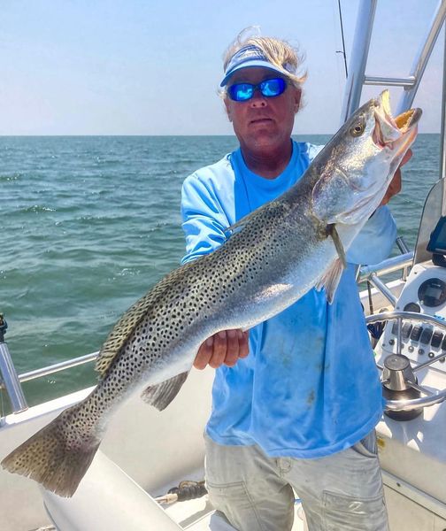 A person holds up a large spotted fish they caught on a fishing charter in Outer Banks, NC.