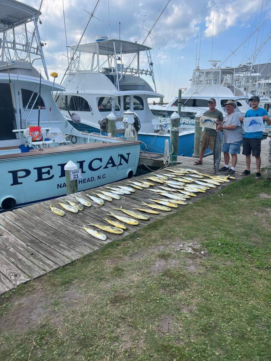 Three people stand on the dock next to a fishing charter in Outer Banks, NC with their catch.