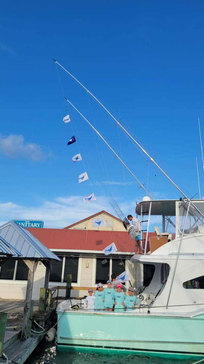 A group of children in matching blue t-shirts smiles on the back of a fishing charter in Outer Banks, NC.