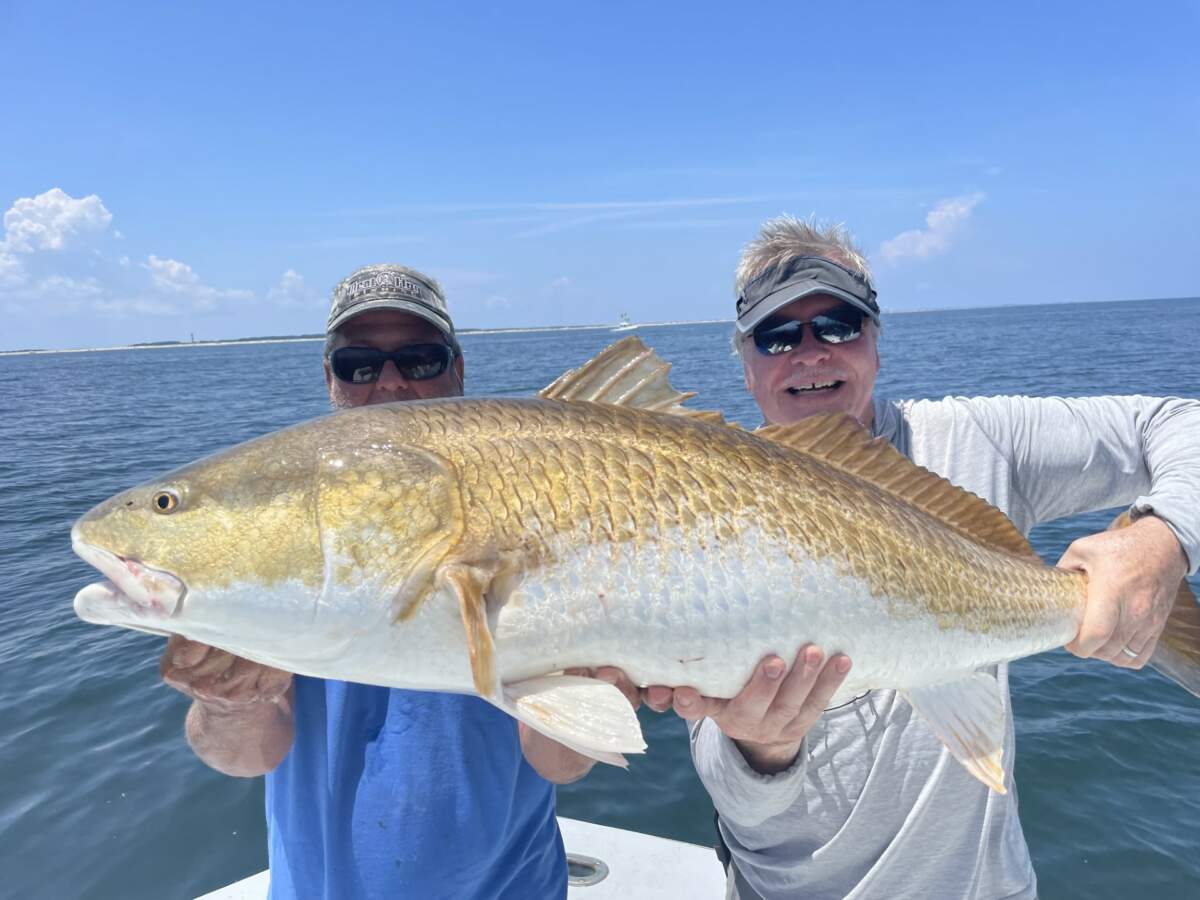 Two people proudly hold up a large gold fish they caught on a fishing charter in Outer Banks, NC.